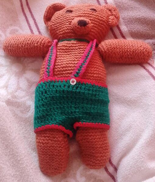 Bild 1 gehäkelter Teddybär, der eine grüne Latzhose trägt