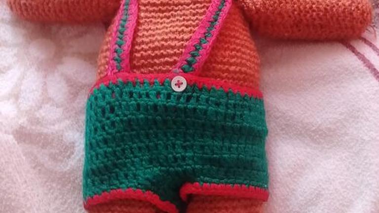 gehäkelter Teddybär, der eine grüne Latzhose trägt